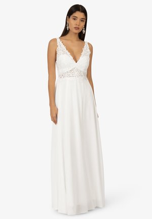 Weißes Maxikleid mit tiefem V-Ausschnitt, Spitzenverzierungen am Oberteil und fließendem Rock; hat dünne Träger und eine glatte Textur.