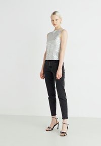 Sølv paljetttopp med høy hals, parret med svarte skinny jeans og svarte stroppestiletter med prikkete detaljer.