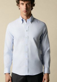 Hellblau gestreiftes Hemd mit langen Ärmeln, button-down Kragen und weißen Knöpfen. Hergestellt aus glattem Stoff mit taillierter Passform.