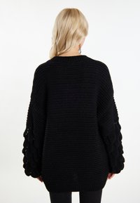 Maglione nero lavorato a maglia, oversize, con maniche a scalloped texturate e scollo rotondo, che presenta una vestibilità ampia e orlo a costine.