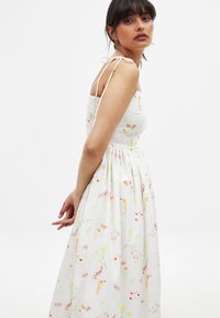 Vestido blanco de flores con un corsé ajustado y una falda fluida. Presenta tirantes delicados y un vibrante patrón de flores dispersas en varios colores.