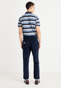 Polo a righe nei colori blu, beige e navy con colletto. Pantaloni di velluto a coste navy con tasche laterali e una piccola etichetta logo sul retro.