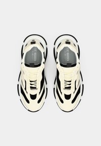 Zapatillas blancas y negras con parte superior de malla, diseño texturizado, cordones visibles y suela en capas. Incluye una etiqueta con el logo en la lengüeta.
