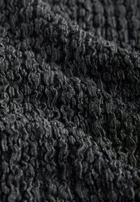 Gros plan d’un tissu noir avec un motif texturé, ondulé et en relief créant un effet tridimensionnel.