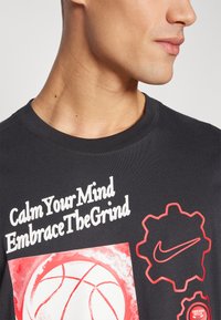 Camiseta de algodón negra con cuello redondo, elementos gráficos rojos y texto blanco con frases motivacionales y diseños temáticos deportivos.