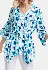 Lätt, blå och aqua-mönstrad blus med V-ringning, trekvartslånga ärmar, insamlad midja med dragsko och asymmetrisk nederkant.