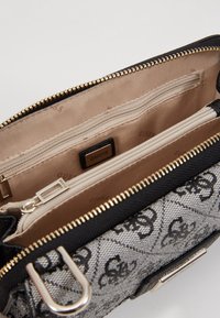 Bolso de mano de patrón negro y gris con cremallera y acentos dorados, que cuenta con un interior beige con múltiples bolsillos y un detalle de logo.