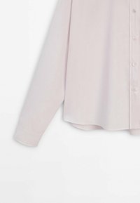 Chemise rose clair à manches longues avec boutons, ourlet incurvé et manches retroussées, présentée sur un fond blanc.