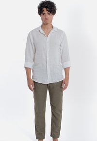 Biała lniana koszula z podwiniętymi rękawami, z zapięciem na guziki z przodu, zestawiona z khaki spodniami. Materiał ma lekki, teksturowany wygląd.