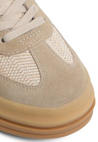 Jasno beżowe sneakersy z zamszu i tkanej tkaniny, z okrągłym czubkiem, beżowymi sznurowadłami i gumową podeszwą.