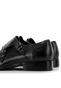 Schwarze Leder Schuhe mit einem eleganten Design, das über doppelte silberne Schnallen und dekorative Lochungen im Obermaterial verfügt, sowie einer glatten, glänzenden Oberfläche.
