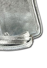 Sac en bandoulière métallique argenté avec une finition texturée, de forme rectangulaire et une fine sangle réglable attachée par un fermoir en métal.