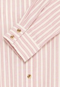 Gros plan sur le poignet d'une chemise rayée rose et blanche avec deux boutons beiges et des rayures assorties sur le corps de la chemise.