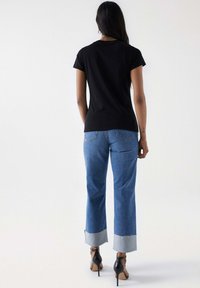 Schwarzes Kurzarm-T-Shirt kombiniert mit hellblauen Schlagjeans, die einen kontrastierenden Denim-Aufschlag aufweisen, und schwarzen High Heels.