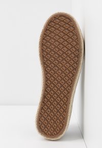 Sole di una scarpa con una superficie in gomma marrone texture, circondata da un bordo in fibra naturale intrecciata, che mostra un design a motivo diamante.