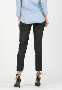 Black fitted pants made of smooth fabric, featuring a tapered design. Paired with black high-heeled shoes with ankle ties and a light blue shirt.