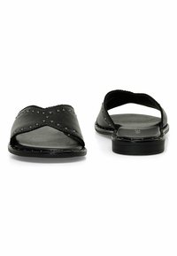 Le ciabatte in pelle nera presentano un design a strap incrociate con dettagli in rivetti, plantare texturizzato e un retro aperto per una facile vestibilità.