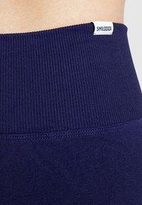 Granatowe legginsy o wysokim stanie z teksturą prążkowaną. Posiadają biały metkę z napisem "SMILODDX" w talii. Gładki materiał.