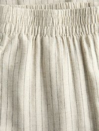 Tessuto beige chiaro con strisce nere verticali; vita elastica arricciata; morbida texture; vista ravvicinata che mette in evidenza i dettagli del tessuto.