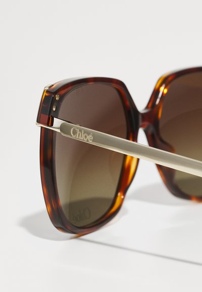 Skildpadde-solsorter med brune linser, geometrisk stel, guldaccent på templet indgraveret med "Chloé." Glat materiale med en glansfuld overflade.