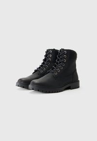 Botas de tobillo con cordones negras, hechas de cuero, con puntera redonda, cuello acolchado y suela de goma texturizada con surcos profundos.