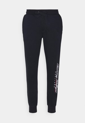 Pantalon de survêtement noir à cordon de serrage avec jambes fuselées et logo "Tommy Hilfiger EST. 1985" sur le mollet droit.