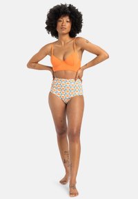 Top de bikini naranja con tirantes ajustables, acompañado de una parte inferior de talle alto que presenta un colorido patrón geométrico de soles y colores pastel.