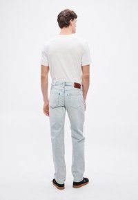 Svijetlo plave traperske traperice ravnog kroja s kožnim smeđim poprečnim žigom na stražnjem dijelu struka i diskretnim stražnjim džepovima.