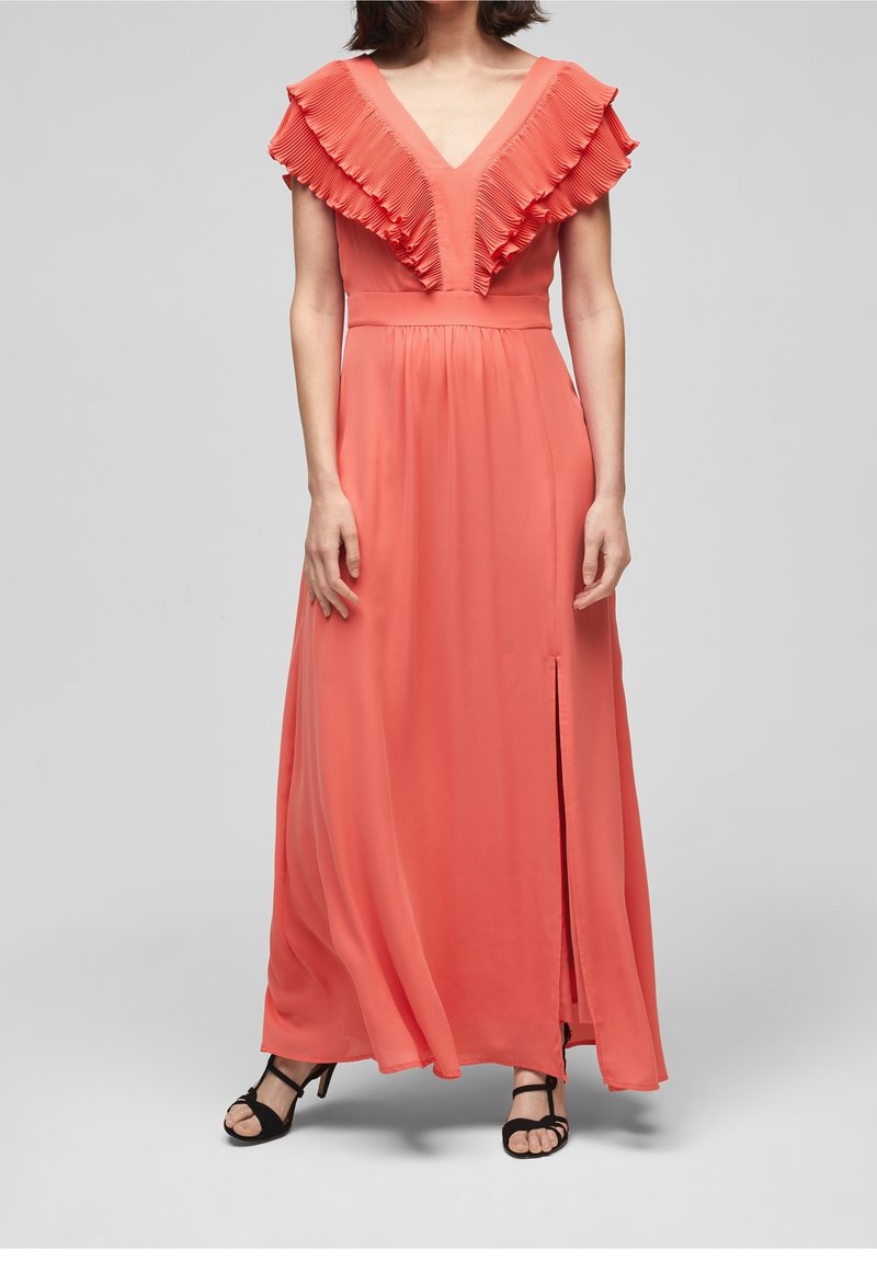 Femme portant une robe maxi corail avec un col en V à volants et une fente devant, associée à des sandales à talons hauts noires à brides.