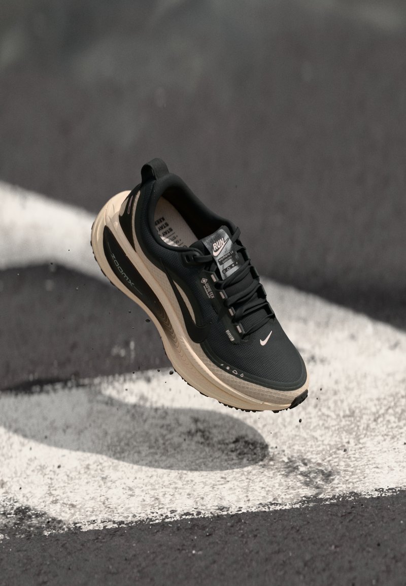 Baskets de sport noires avec une tige texturée, un talon surélevé et une semelle intermédiaire beige. Équipées de lacets, d'un logo sur le côté et d'une semelle intérieure rembourrée.