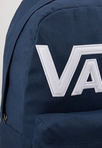 Zaino in tessuto blu navy con logo bianco in rilievo. Superficie testurizzata con una tasca frontale e cuciture rinforzate lungo i bordi.