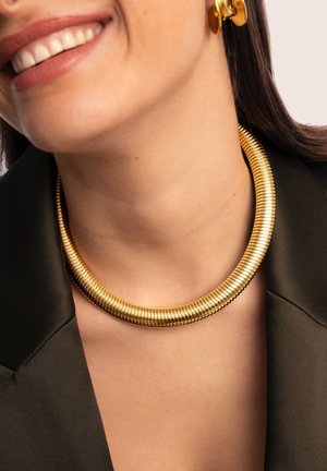 Collana choker color oro con design a spirale, caratterizzata da una finitura metallica liscia e una forma circolare flessibile. Indossata vicino al collo.