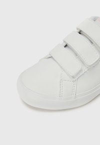 Fehér sneaker sima szintetikus felsőrésszel, három tépőzárral, lekerekített orral és tapadós gumitalppal.