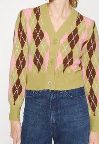 Stickad cardigan med V-ringning, grön bas med rosa, brun och vit diamantmönster, samt knäppning fram. Ribbad fåll och ärmslut.