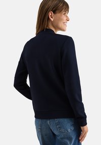 Maglione a righe navy con colletto tondo e maniche lunghe, caratterizzato da un orlo a coste. Abbinato a jeans azzurri, visto da dietro.