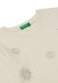Cremefarbendes Baumwoll-T-Shirt mit silbernen Strass-Schneeflocken-Designs auf der Vorderseite, Rundhalsausschnitt und grünem Etikett.