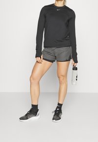 Černé dlouhé rukávy sportovní top, šedé šortky s černým lemem, černo-bílé běžecké boty, průhledná lahev na vodu. Minimalistický design, funkční střih.