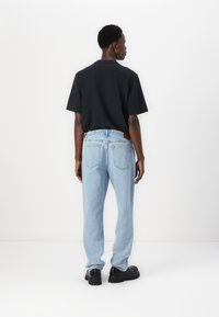 Jeans de mezclilla azul claro con un corte holgado, bolsillos traseros y una etiqueta de marca de cuero marrón, combinados con una camiseta negra de manga corta.