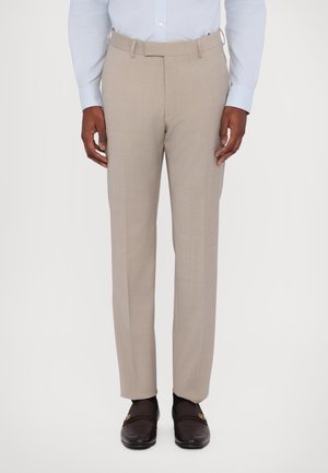 Pantaloni beige su misura con una texture liscia, davanti piatto e tasche laterali. Indossati con una camicia azzurro chiaro e mocassini scuri.