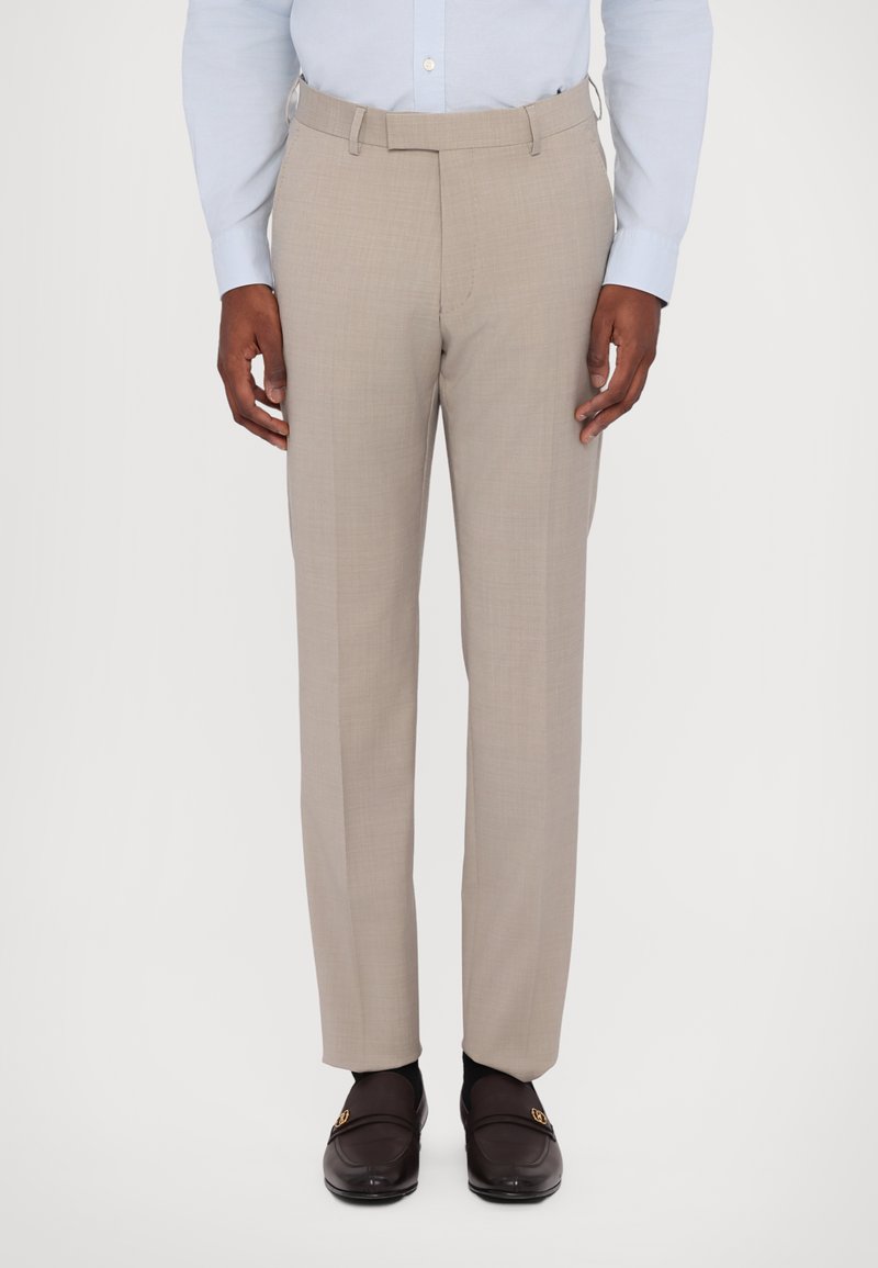 Beige tailored trousers with a smooth texture, flat front, and side pockets. Worn with a light blue shirt and dark loafers.