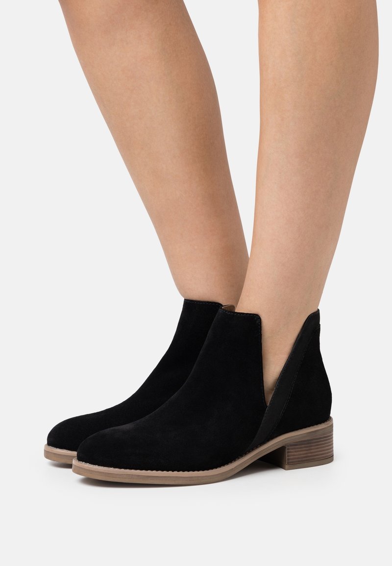 Bottines en daim noir avec un petit talon bloc, découpes latérales et une texture lisse, dotées d'une semelle claire et d'un bord cousu.