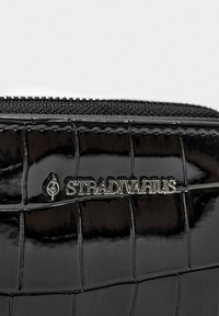Portefeuille en simili cuir patiné noir avec motif crocodile, matériel argenté et fermeture éclair. Présente le logo "Stradivarius" en lettres métalliques.