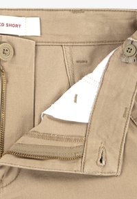 Χακί σορτς με φερμουάρ, κούμπωμα με κουμπί και εσωτερική ετικέτα. Το ύφασμα έχει λεία υφή και διαθέτει διακριτική πλαϊνή τσέπη.