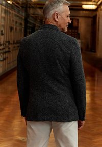 Blazer texturizado gris con un diseño ajustado, que presenta una abertura trasera y puños abotonados, combinado con pantalones de color claro.