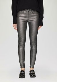 Metaliczne srebrne jeansy typu skinny z subtelnym połyskiem, z klasycznym pięciopocketowym designem i standardowym pasem, połączone z czarnymi loafersami.