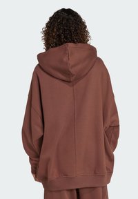 Brązowy, oversize'owy hoodie z kapturem na sznurki, długimi rękawami i ribbowymi mankietami. Gładka tekstura z widocznymi detalami szwów na plecach.
