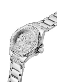 Montre Guess en argent avec un boîtier octogonal, des accents en cristal, trois sous-cadrans et un bracelet en métal poli. Cadran texturé avec le logo de la marque.