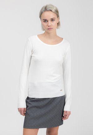 Weißer Pullover mit langen Ärmeln, rundem Halsausschnitt und geripptem Saum, kombiniert mit einem grauen Rock mit weißen Punkten und gerader Schnittführung.