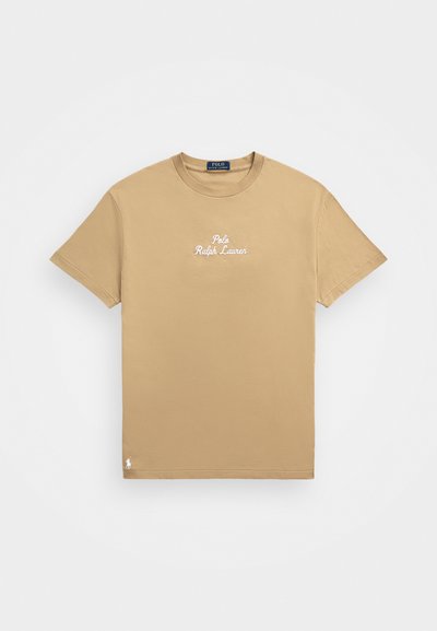 Tričko s krátkym rukávom, s okrúhlym výstrihom, vyrobené z hnedé bavlny. Obsahuje vyšívaný text "Polo Ralph Lauren" na hrudi a malé logo na leme.