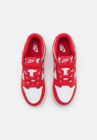 Raudoni ir balti Nike sportbačiai su odiniu ir tinkliniu viršumi, suapvalinta nosimi, perforuotais elementais ir plokščiomis raištelėmis. Išsiskiriantis logotipas ant liežuvio.